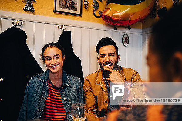 Lächelnder junger Mann und lächelnde junge Frau  die eine Freundin während einer Dinnerparty im Restaurant anschauen