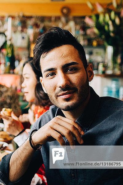 Porträt eines selbstbewussten jungen Mannes  der während einer Dinnerparty im Restaurant am Tisch sitzt