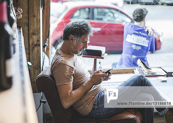 Mature owner using mobile phone while sitting on chair in deli