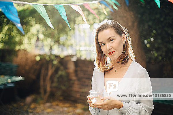 Porträt einer jungen Frau  die ein Getränk in der Hand hält  während sie im Hinterhof steht