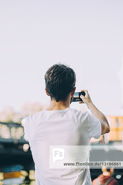 Rear view of young man photographing through mobile phone while standing on street