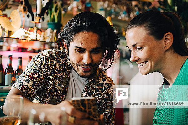 Lächelnder junger Mann teilt sein Smartphone mit einer Frau  die während der Brunch-Party im Restaurant sitzt