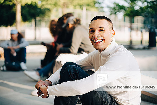 Portrait of happy young man sitting with friends at skateboard park