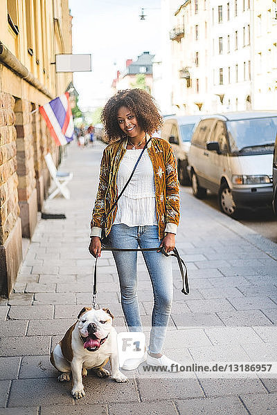 Porträt einer lächelnden  mittelgroßen  erwachsenen Frau mit Hund auf dem Bürgersteig in der Stadt