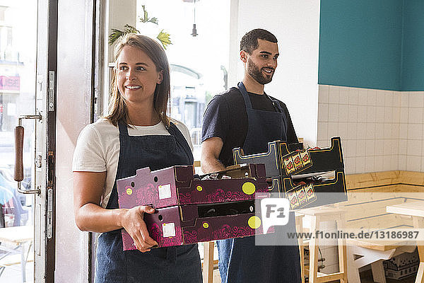 Lächelnder multiethnischer Verkäufer und Verkäuferin beim Tragen von Kisten im Restaurant