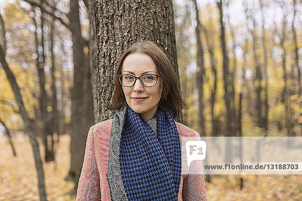 Portrait confident woman in scarf standing against tree in autumn park