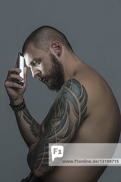 Portrait serious bare chested man with tattoos holding smart phone