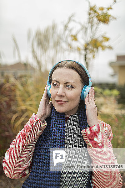 Lächelnde Frau  die draußen mit Kopfhörern Musik hört