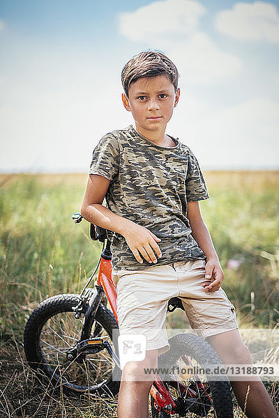 Portrait serious boy on bicycle in field