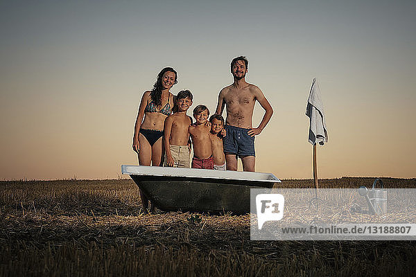 Porträt einer lächelnden Familie in Badeanzügen  die neben einer Badewanne in einem ländlichen Gebiet steht