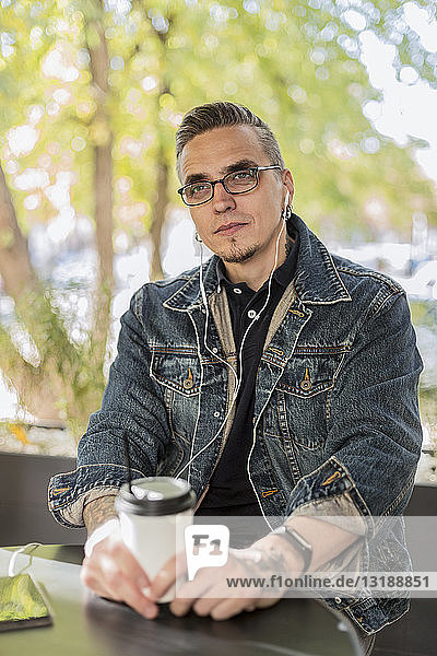 Man listening to music with earbuds drinking coffee in cafe