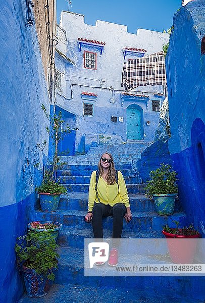 Junge Frau sitzt auf Treppe in der Altstadt blaue Hausfassaden Medina von Chefchaouen Chaouen Tanger-Tétouan Marokko Afrika