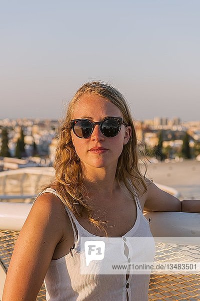 Junge Frau mit weißem Oberteil und Sonnenbrille schaut in die Kamera  Plaza de la Encarnacion  hinter Häusern  Sevilla  Andalusien  Spanien  Europa