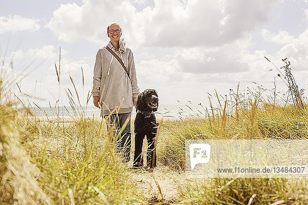 Woman walks with her dog  king poodle  in the dunes by the sea  Portbail  Normandy  France  Europe