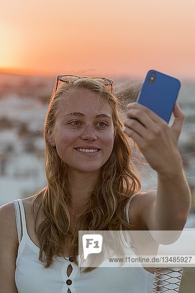 Junge Frau mit weißem Top fotografiert sich selbst mit einem Smartphone Portrait Selfie Sonnenuntergang Plaza de la Encarnacion Sevilla Andalusien Spanien Europa