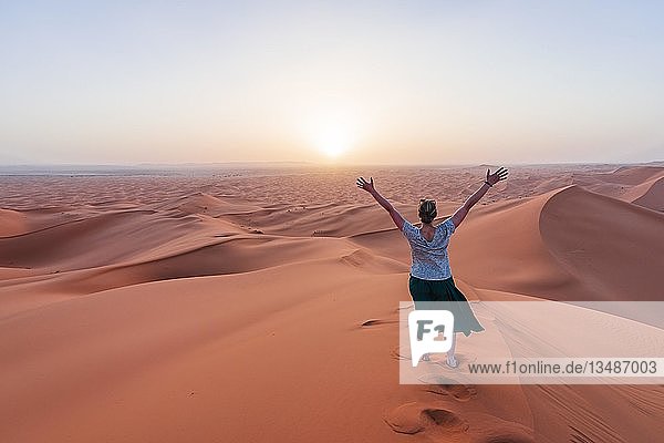 Wanderin streckt Arme in die Luft  rote Sanddüne in der Wüste  Sonnenuntergang  Erg Chebbi  Merzouga  Sahara  Marokko  Afrika