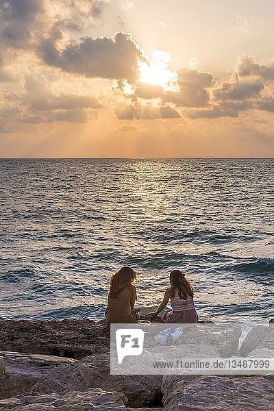 Zwei Frauen sitzen bei Sonnenuntergang auf Felsen und blicken auf das Meer  Tel Aviv  Israel  Asien