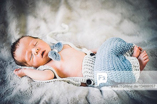 A newborn baby boy sleeping in blue and grey knitted bow tie and trousers  Portugal  Europe