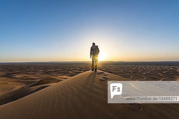Junger Mann steht auf einer Sanddüne  Sonnenaufgang  Erg Chebbi  Merzouga  Sahara  Marokko  Afrika