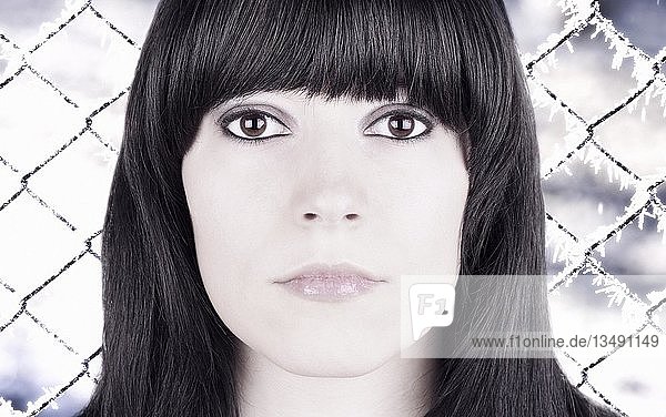 Porträt eines Mädchens mit schwarzen Haaren und braunen Augen vor einem mit Eiskristallen bedeckten Maschendrahtzaun