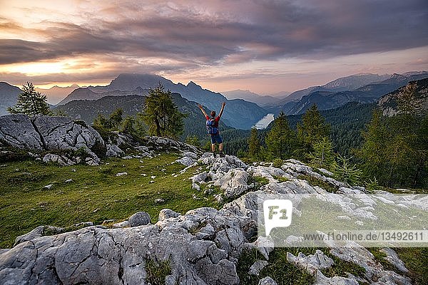 Hiker stretches his arms into the air  summit of Feldkogel  view of KÃ¶nigssee at sunset  left Watzmann SÃ¼dspitze and Watzmannkinder  Berchtesgaden National Park  Berchtesgadener Land  Upper Bavaria  Bavaria  Germany  Europe