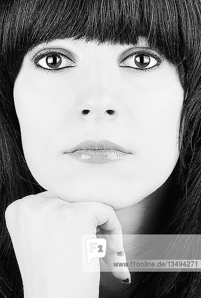 Porträt eines Mädchens mit schwarzen Haaren und großen Augen  das sein Kinn auf die Hand stützt  schwarz-weiß