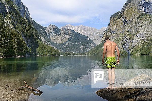 Young man in swimming trunks stands on a stone in Lake Obersee  mountain lake  mountain landscape  in the back Watzmann massif  Salet am Königssee  Berchtesgaden National Park  Berchtesgadener Land  Upper Bavaria  Bavaria  Germany  Europe
