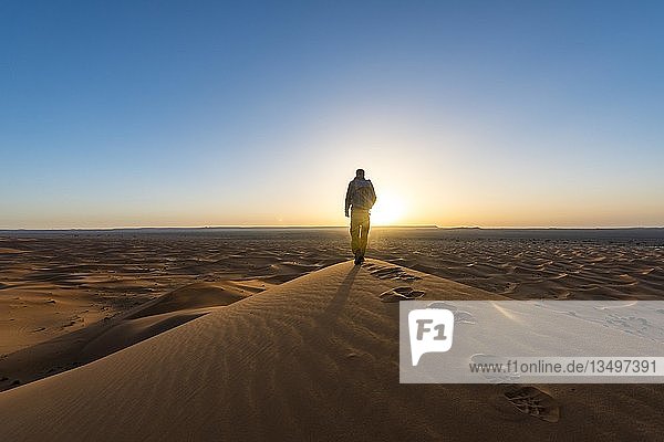 Junger Mann steht auf einer Sanddüne  Sonnenaufgang  Erg Chebbi  Merzouga  Sahara  Marokko  Afrika