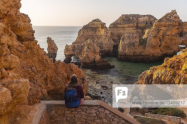 Wanderin sitzt auf Steinmauer und schaut über Felsen ins Meer  Algarve Felsenküste  Ponta da Piedade  Lagos  Portugal  Europa
