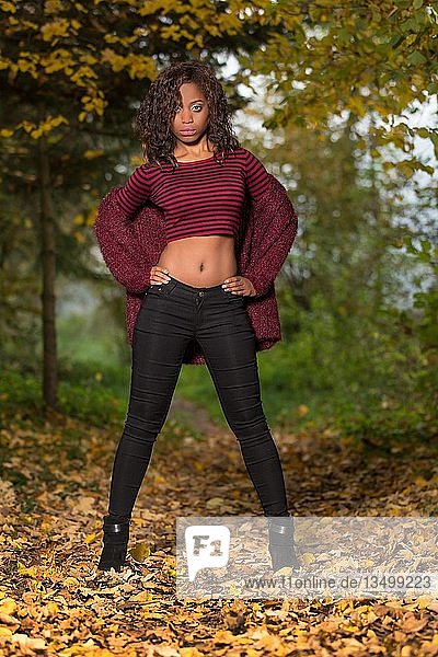 Dark-skinned young woman with belly top in autumn forest