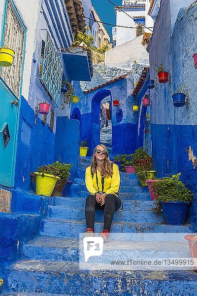 Junge Frau in der Altstadt sitzt auf einer Treppe  blaue Hauswände  Medina von Chefchaouen  Chaouen  Tanger-Tétouan  Königreich Marokko