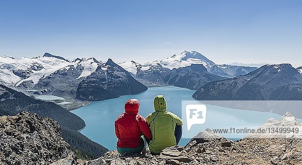 Blick vom Panorama Ridge Trail  Zwei Wanderer sitzen auf einem Felsen mit Garibaldi Lake  türkisfarbener Gletschersee  Guard Mountain und Deception Peak  Rückengletscher  Garibaldi Provincial Park  British Columbia  Kanada  Nordamerika