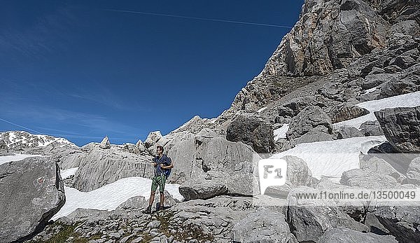 Hiker among rocks and snow remains  hiking trail to Wasseralm over Niederbrunnsulzen  Steinernes Meer  Berchtesgaden National Park  Bavaria  Germany  Europe