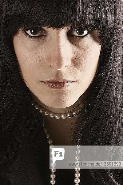 Porträt eines Mädchens mit schwarzen Haaren und braunen Augen  das eine Perlenkette trägt