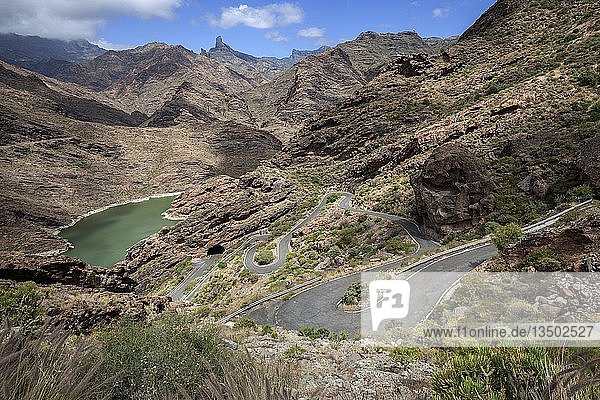 Volcanic barren mountain landscape with a view of the reservoir Presa del Parralillo  winding road GC606  at El Carrizal  behind cult rock Roque Bentayga  Gran Canaria  Canary Islands  Spain  Europe