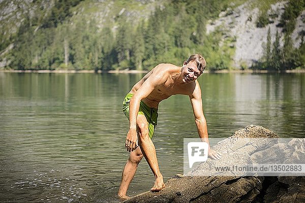 Young man with bathing trunks  climbs on stone  Lake Obersee  mountain lake  mountain landscape  Salet am Königssee  Berchtesgaden National Park  Berchtesgadener Land  Upper Bavaria  Bavaria  Germany  Europe