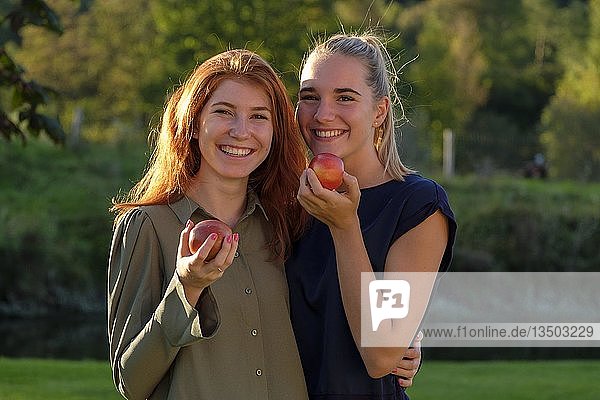 Zwei Mädchen  junge Frauen  lachend Äpfel essend  im Garten  Oberbayern  Bayern  Deutschland  Europa