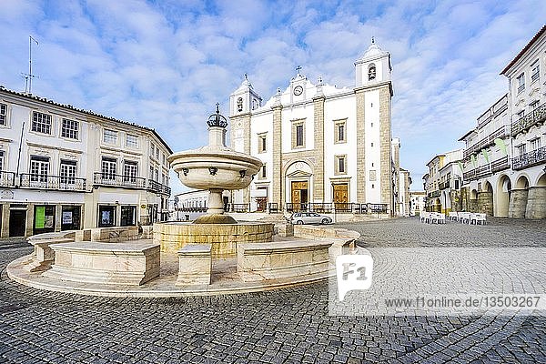 Niedrigwinkelaufnahme eines Brunnens  umgeben von traditionellen Wohngebäuden und mit der Kirche Saint Anton im Hintergrund  Giraldo-Platz  Evora  Alentejo  Portugal  Europa