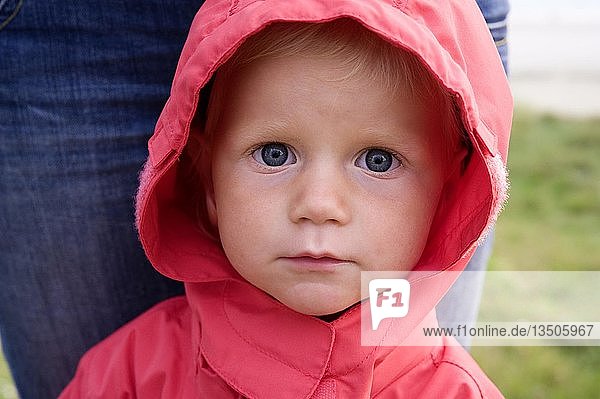 Porträt eines kleinen Mädchens mit roter Regenjacke  hinter ihr die Mutter