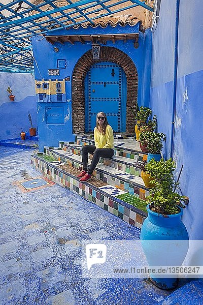 Junge Frau in der Altstadt sitzt auf einer Treppe Blaue Hauswände Medina von Chefchaouen Chaouen Tanger-Tétouan Marokko Afrika