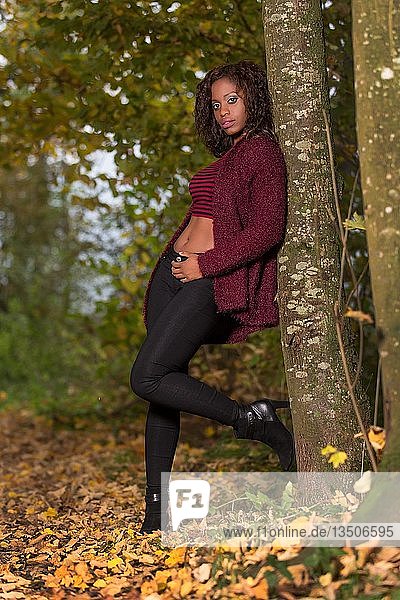 Dunkelhäutige junge Frau mit bauchfreiem Oberteil im Herbstwald