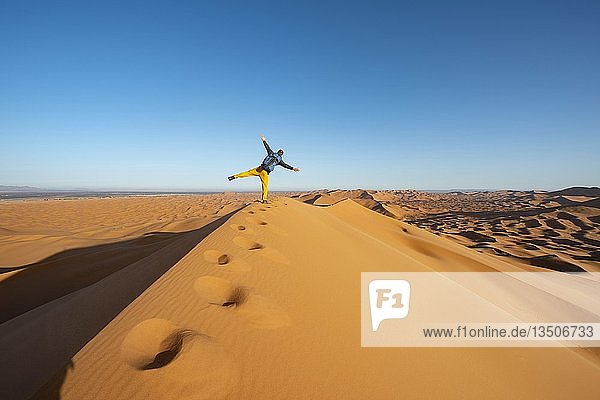 Junger Mann auf Sanddüne  auf einem Bein stehend  Erg Chebbi  Merzouga  Sahara  Marokko  Afrika
