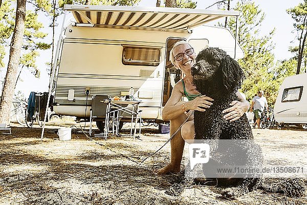 Frau hockt lachend mit ihrem Hund  Königspudel  vor einem Wohnmobil auf einem Campingplatz  le Gurp  Grayan-et-l`Hopital  Aquitaine  Gironde  Frankreich  Europa