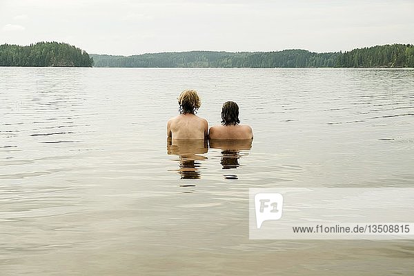 Zwei junge Frauen sitzen im Wasser und schauen in die Ferne  Gunnern-See  Gunnarskog  Arvika  Värmland  Schweden  Europa