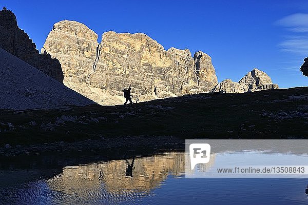 Hiker on the lake in the backlight  below the Paternalsattel  Three Peaks of Lavaredo  with a view of the Zwölferkofel  Hochpustertal valley  Sexten Dolomites  South Tyrol  Italy  Europe