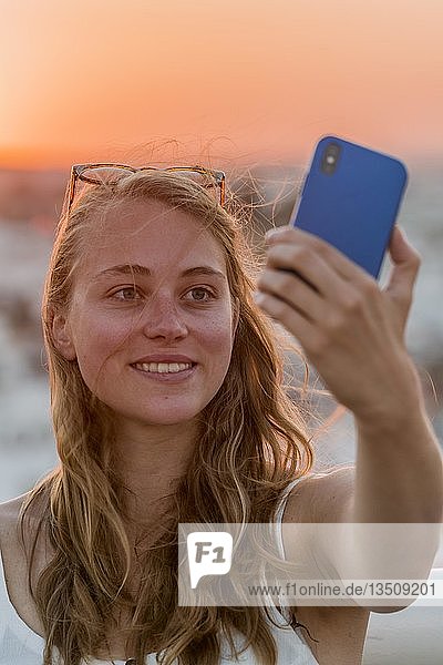 Junge Frau mit weißem Oberteil fotografiert sich selbst mit einem Smartphone  Selfie  Sonnenuntergang  Plaza de la Encarnacion  Sevilla  Andalusien  Spanien  Europa