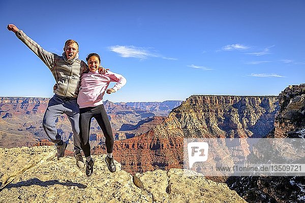 Paar  springend  vor der gigantischen Schlucht des Grand Canyon  Blick vom Rim Trail  zwischen Mather Point und Yavapai Point  erodierte Felslandschaft  South Rim  Grand Canyon National Park  bei Tusayan  Arizona  USA  Nordamerika