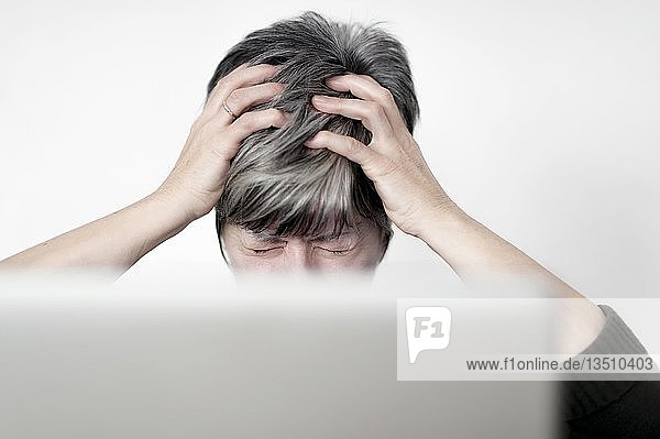 Gestresste Frau  die hinter einem Computerbildschirm sitzt und an ihren Haaren zieht