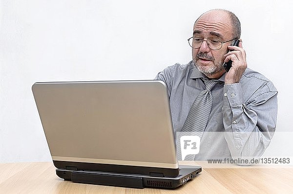 Mann telefoniert  während er an seinem Laptop arbeitet