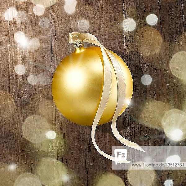 Eine goldene Weihnachtskugel mit Schleife  auf Holzplatte  Lichtreflexe  Lichtsterne und blinde Flecken im Vordergrund  Deutschland  Europa